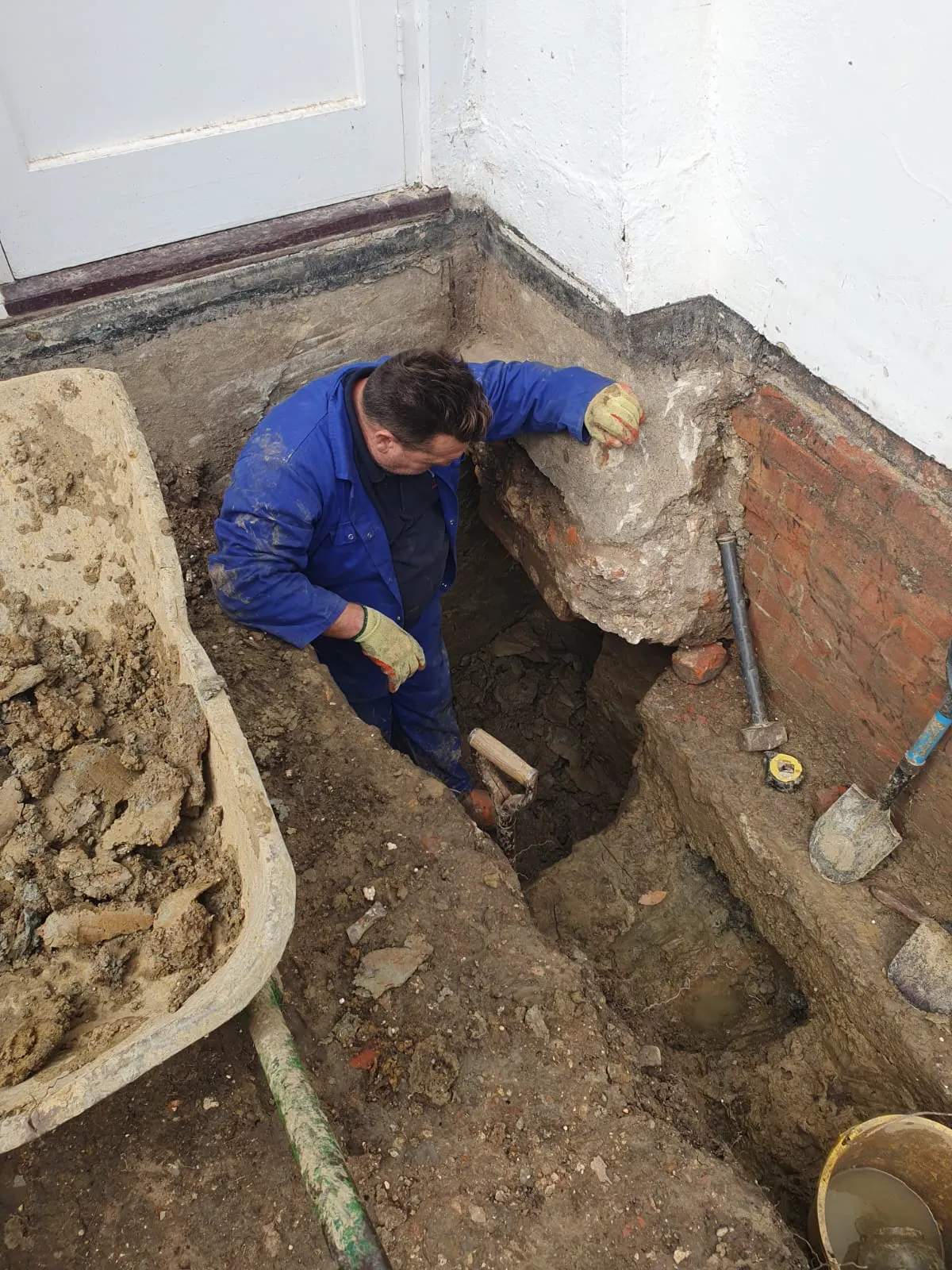 A man in a blue coverall working on a brick wall.
