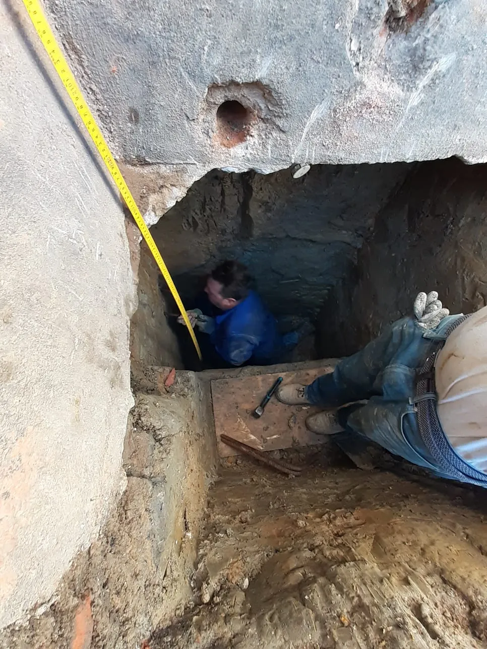 A man sitting in a hole with a measuring tape.