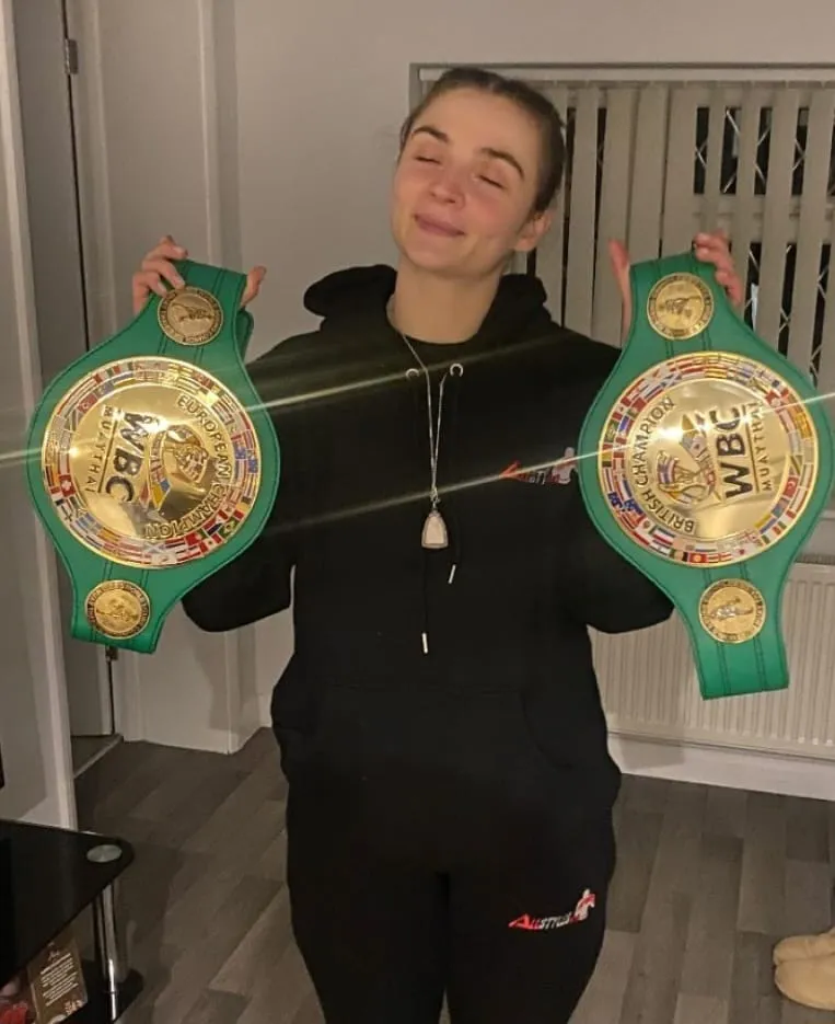 A woman holding two green and gold belts.